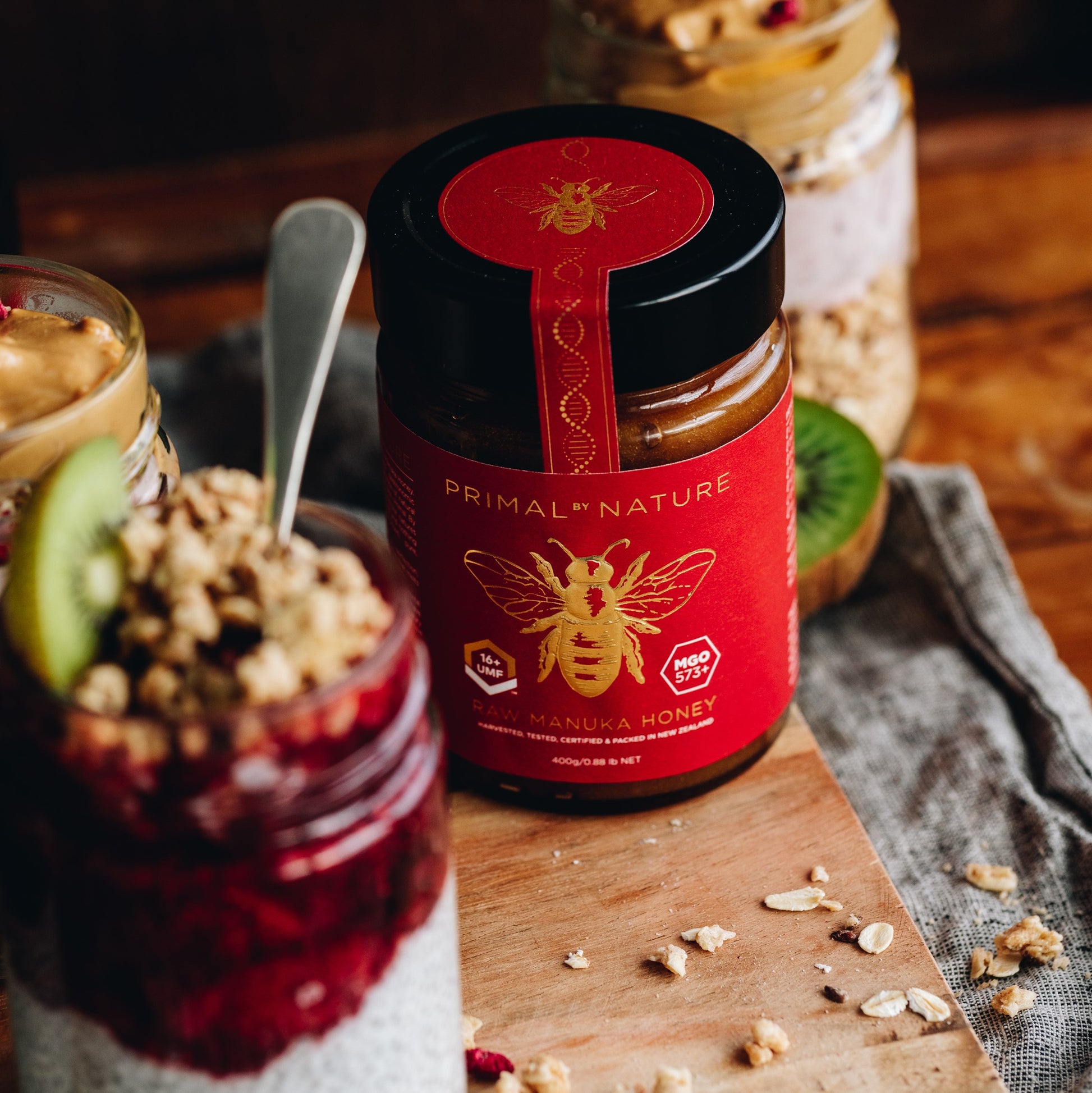 Primal by Nature Glass Jar Genuine 100% Pure Manuka Honey UMF 16+ MGO 573 set on a chopping board surrounded by reused Glass Jars with dessert jars
